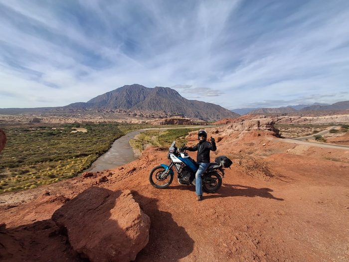 Rider junto a su moto en un mirador sobre el cerro, con el valle de fondo